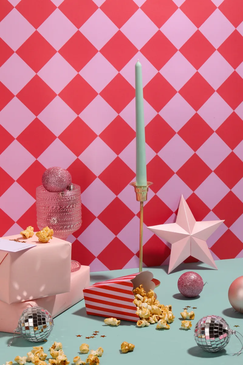 Bodegón de Boreal con caja de regalo, crispetas, bolas de discoteca y una estrella sobre fondo de rombos rosados